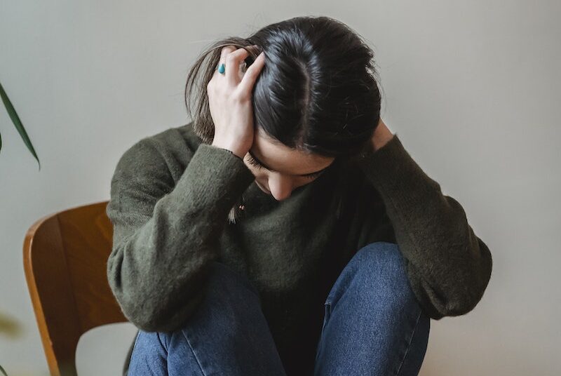 Anxious young woman cover wing ears with hands sitting on chair